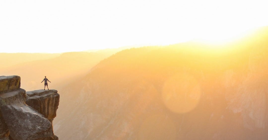 silhouette of person standing on cliff during sunset