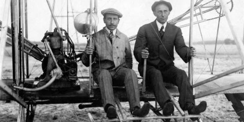 Historic black and white photo of the Wright brothers sitting in their early aircraft Historic black and white photo of the Wright brothers sitting in their early aircraft
