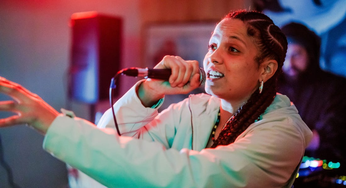A woman wearing a mint green blazer singing into a microphone A woman wearing a mint green blazer singing into a microphone