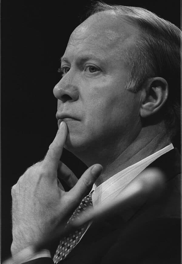 A close-up black and white photo of him seen in profile pressing an index finger against his chin. 