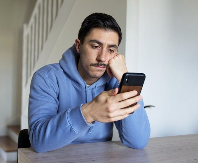 A man sitting at a table looking at a cellphone.