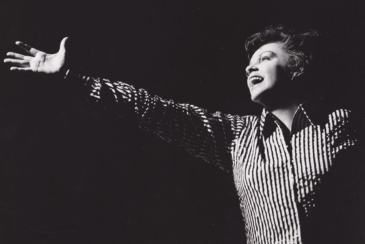 Black-and-white publicity photograph of Judy Garland, arm outreached and standing alone on stage during a performance scene from I Could Go On Singing (1963).
