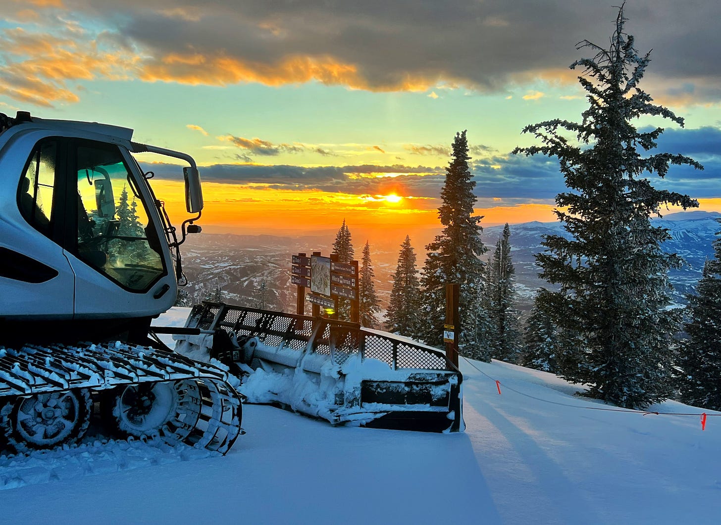 Photo of a snow groomer parked at the top of a ski run at Steamboat Resort overlooking the Yampa Valley at sunset.