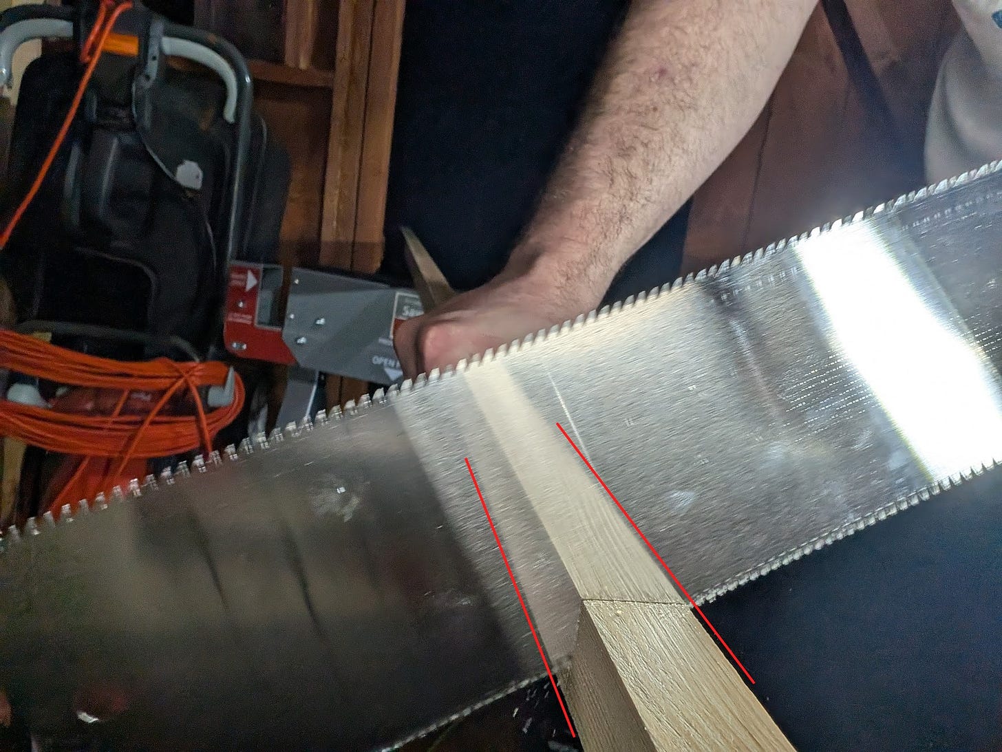 a double edged saw cutting wood at an angle, red marks added to the photo afterward to show how to use the reflection in the surface of the saw blade