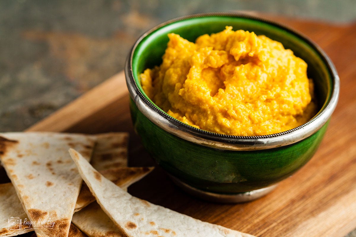 Carrot and goats cheese dip in a green bowl with triangles of flat bread on the side