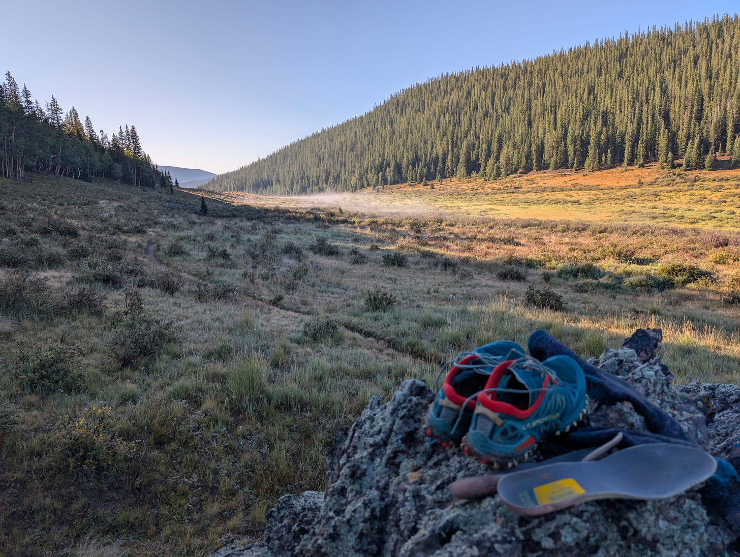 Trail running shoes and insoles resting on a rock at a Colorado Trail campsite, highlighting recovery, foot care, and fatigue management after long descents