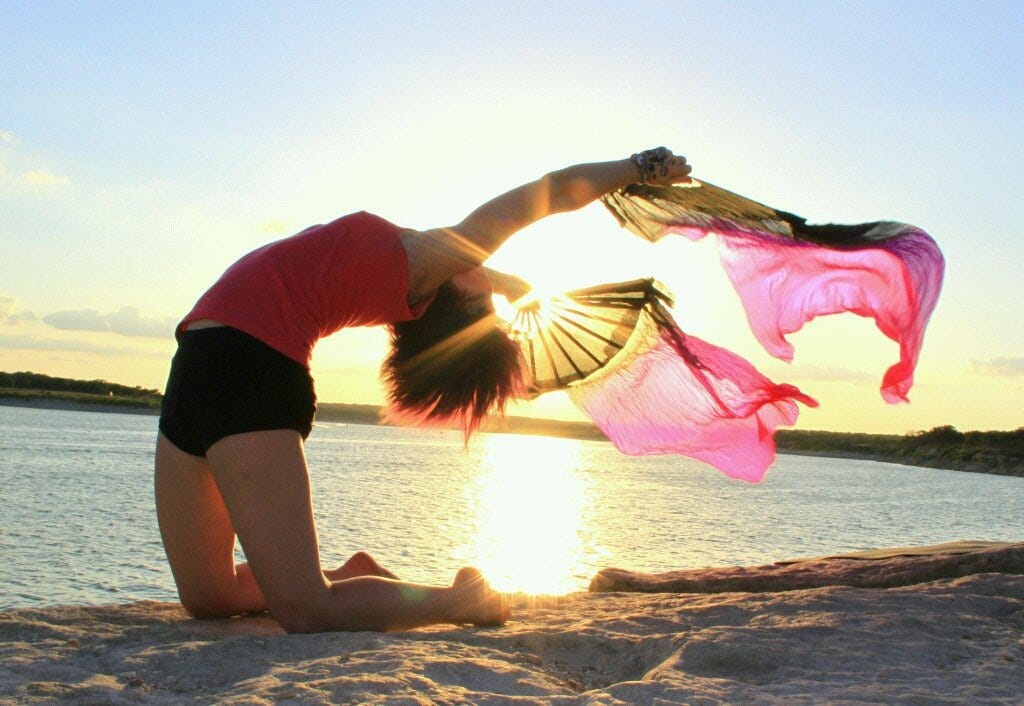 Photo of Lyric at the lake, doing a back bend in the sunset with pink and black silk fans. 