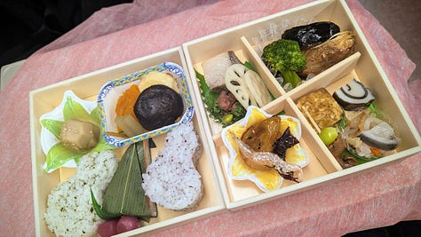 Colorful Japanese dishes inside of an obento lunch box. The box wrapped in a pink furoshiki cloth. An illustrated map inside the cover.