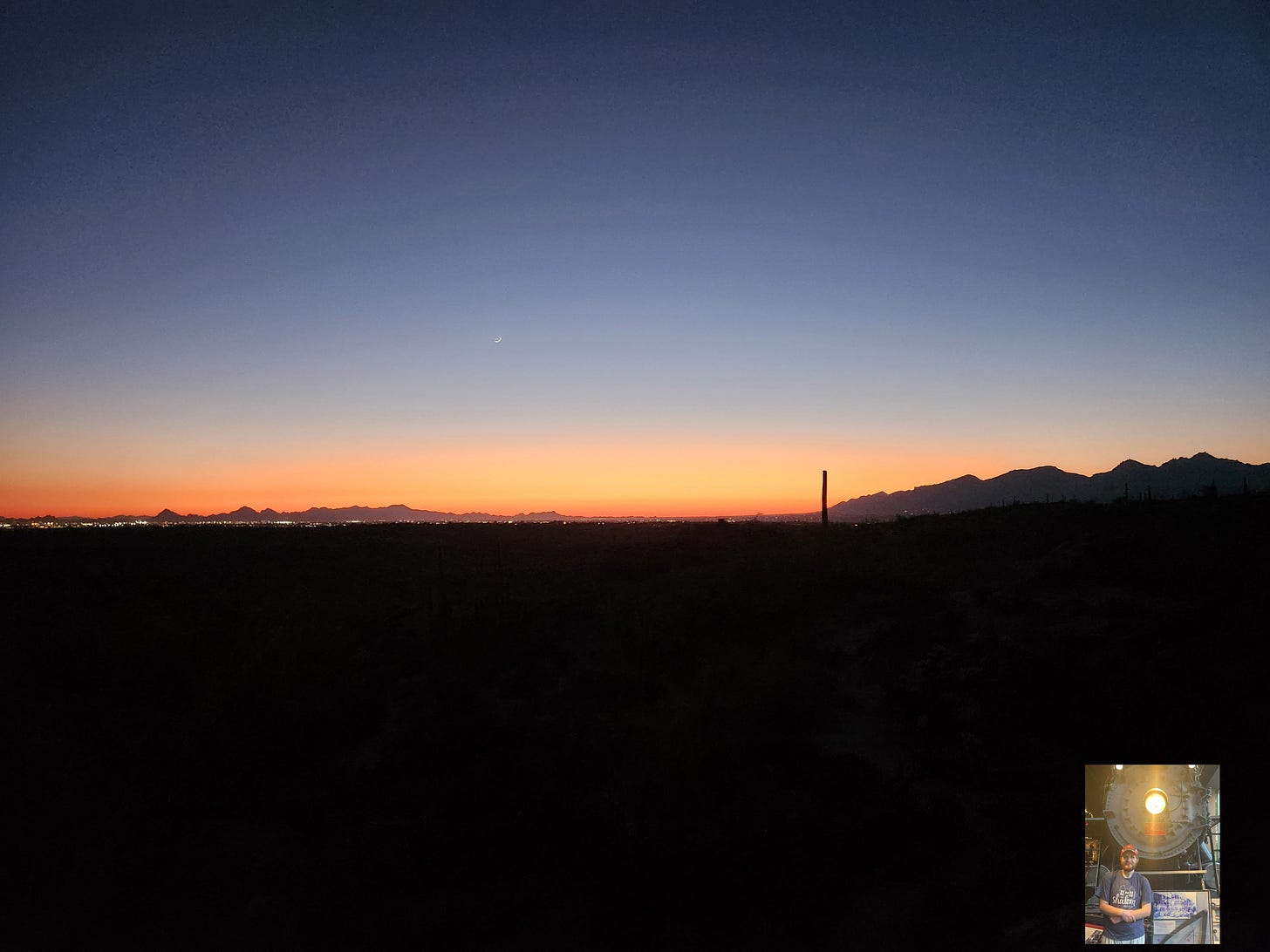 A view of Saguaro National Park at sunset. The sky transitions from dark blue to light blue, then to a pink and orange mix at the bottom.
