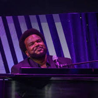 A black man looks pensively into the distance from in front of a grand piano.