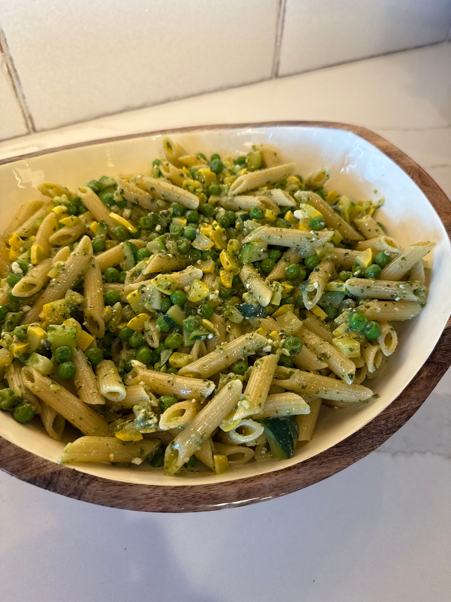 A large white bowl filled with penne pasta mixed with green peas and pesto. A large white bowl filled with penne pasta mixed with green peas and pesto.
