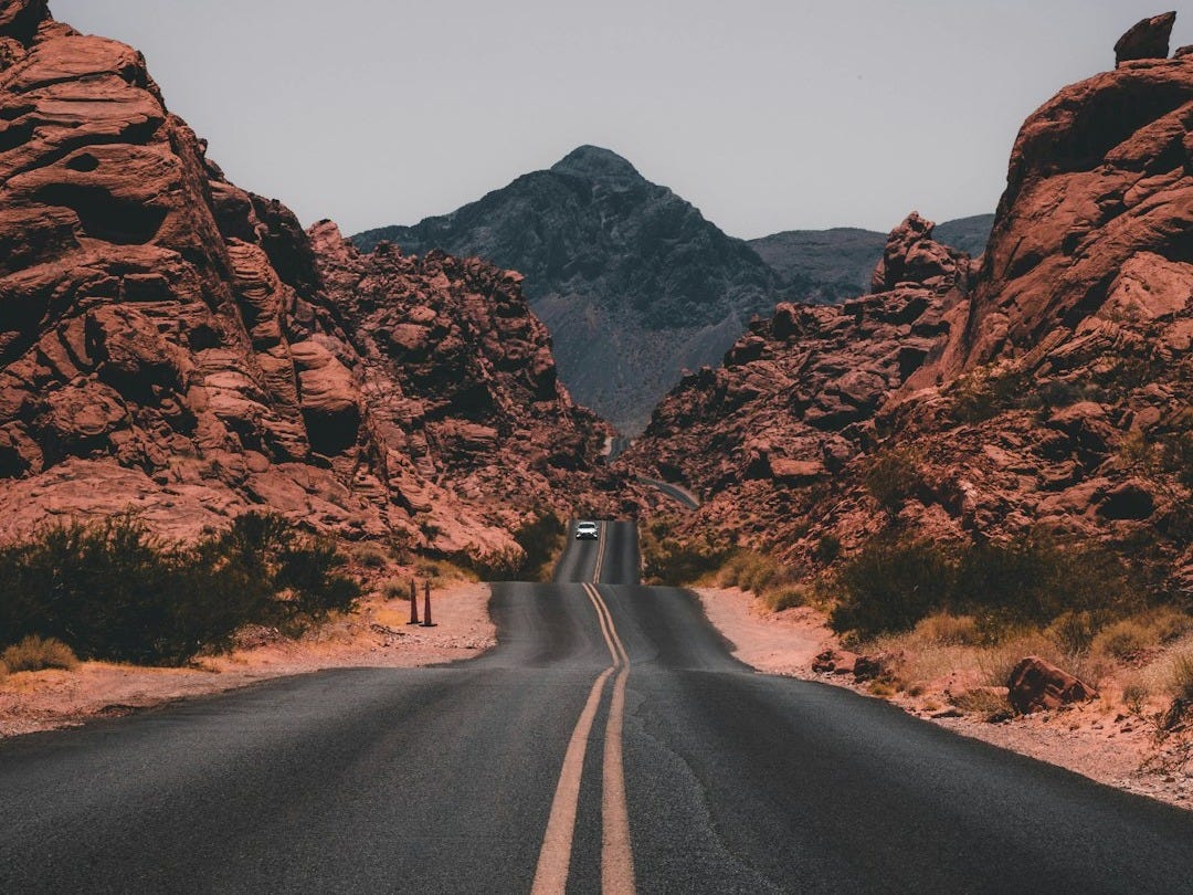 black concrete road surrounded by brown rocks black concrete road surrounded by brown rocks