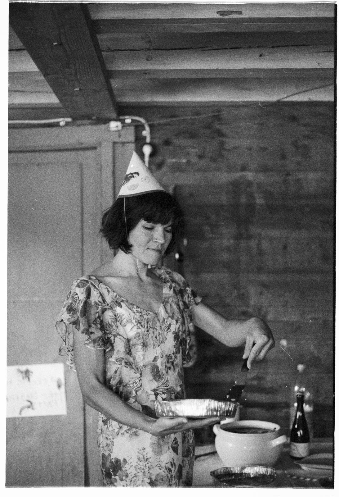Woman dressed in flowery silk dress, wearing a paper party hard adorned with pictures of crayfish, serving slices of Swedish Västerbotten pie at a Swedish crayfish party inside an old boatshed. Woman dressed in flowery silk dress, wearing a paper party hard adorned with pictures of crayfish, serving slices of Swedish Västerbotten pie at a Swedish crayfish party inside an old boatshed.