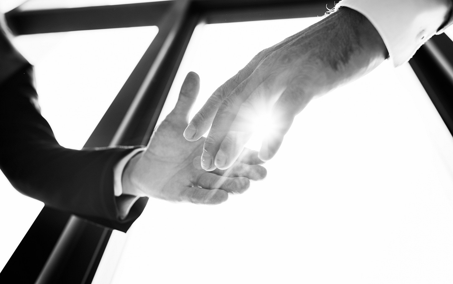 A monochrome close-up of two hands reaching toward each other, with bright light shining between them, symbolizing trust, connection, and the transfer of responsibility. A monochrome close-up of two hands reaching toward each other, with bright light shining between them, symbolizing trust, connection, and the transfer of responsibility.