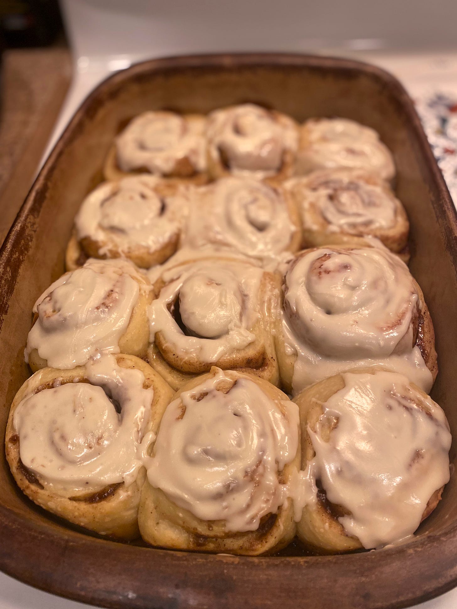 A stoneware pan of a dozen fresh cinnamon buns, the glaze on top still gooey.