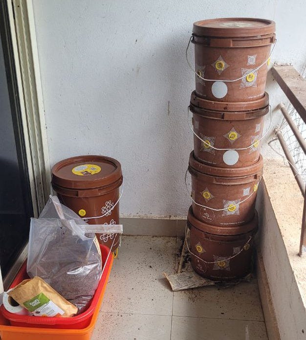in the corner of a balcony are four brown buckets piled on top of each other. In another corner is a larger brown bucket standing on its own.