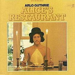 Album cover for Arlo Guthrie's Alice's Restaurant featuring Arlo Guthrie shirtless with a hat on and a napkin attached to his chest, holding a fork and a knife at a Thanksgiving table with candles.
