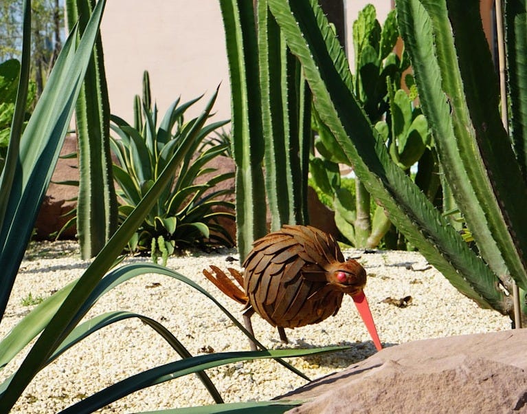 A small rusty bird sculpture in a desert garden