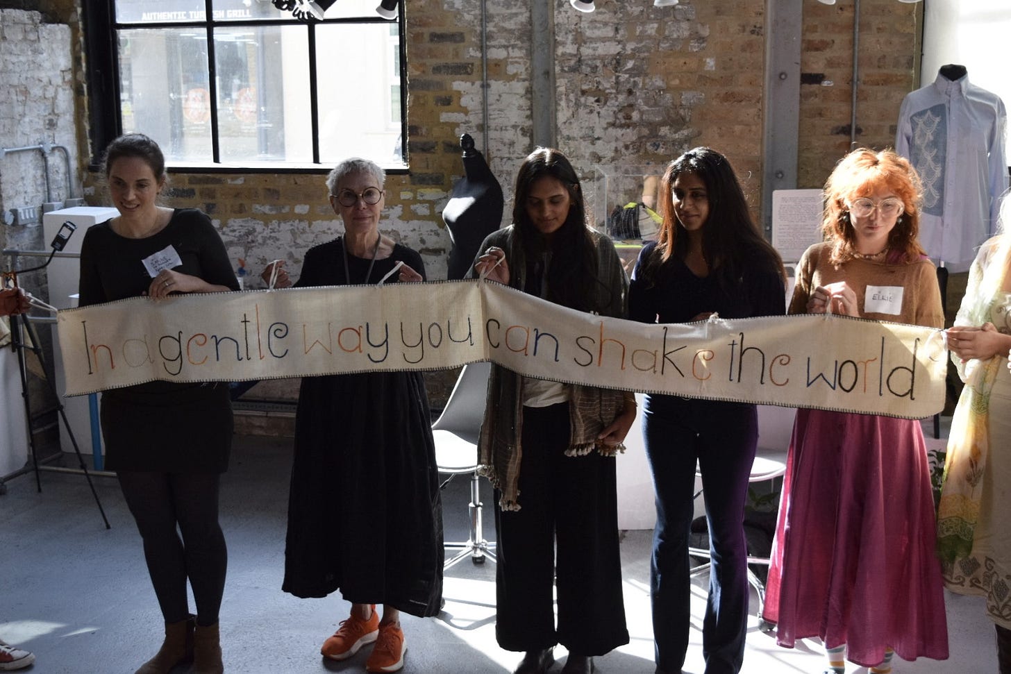 Panellists on day one holding up a banner that says, “In a gentle way you can shake the world.“ [Credit: The Festival of Natural Fibres].