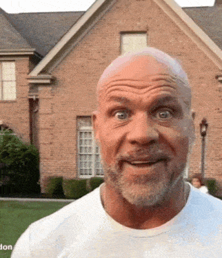 a man with a beard is making a funny face in front of a brick house . a man with a beard is making a funny face in front of a brick house .