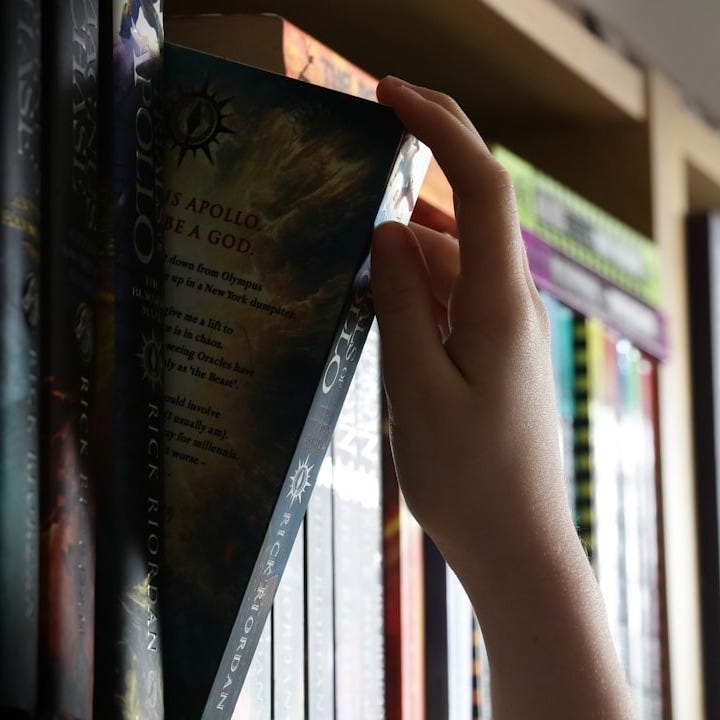 a person holding a book in front of a book shelf