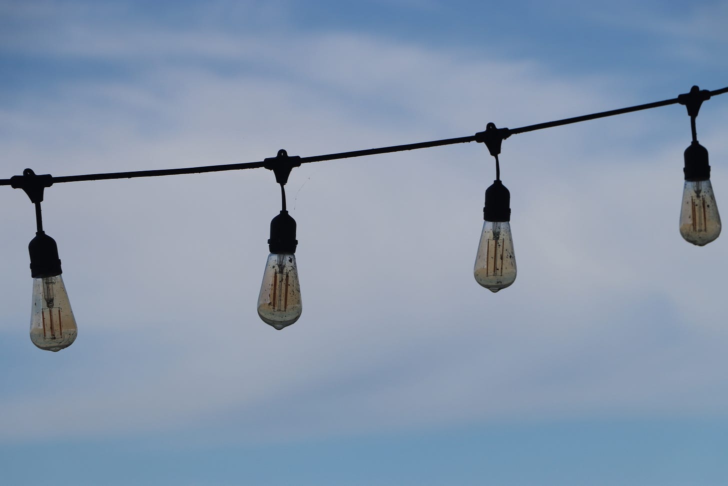 Unlit lights framed against a lightly clouded hazy blue sky