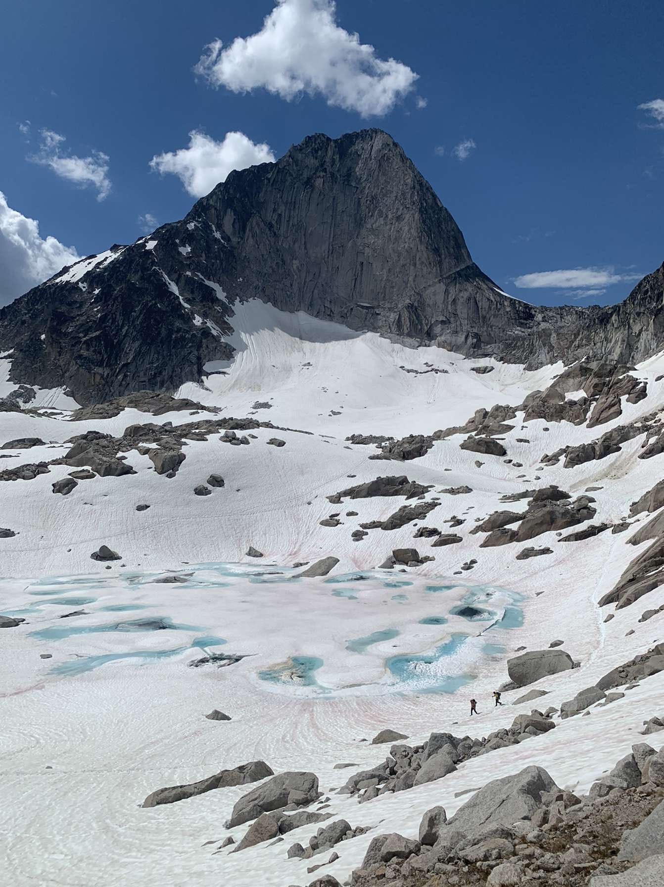 A high mountain peak with a snow covered lake in the valley between the mountains. Two people are walking on the snow in the distance. A high mountain peak with a snow covered lake in the valley between the mountains. Two people are walking on the snow in the distance.