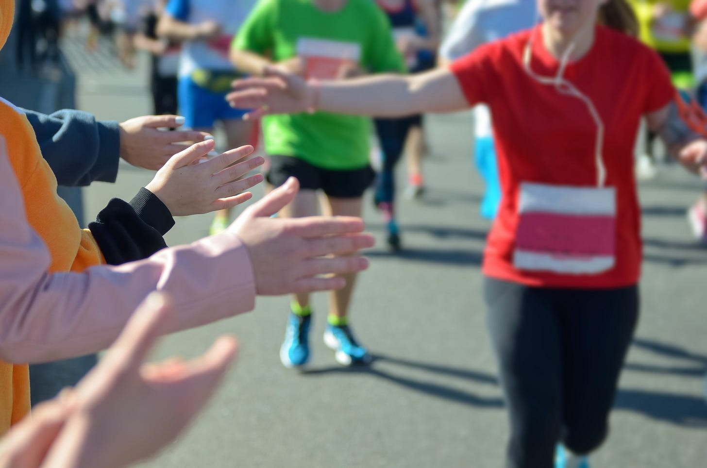 marathon runner in red reaching out her hand to high five three spectators in the foreground