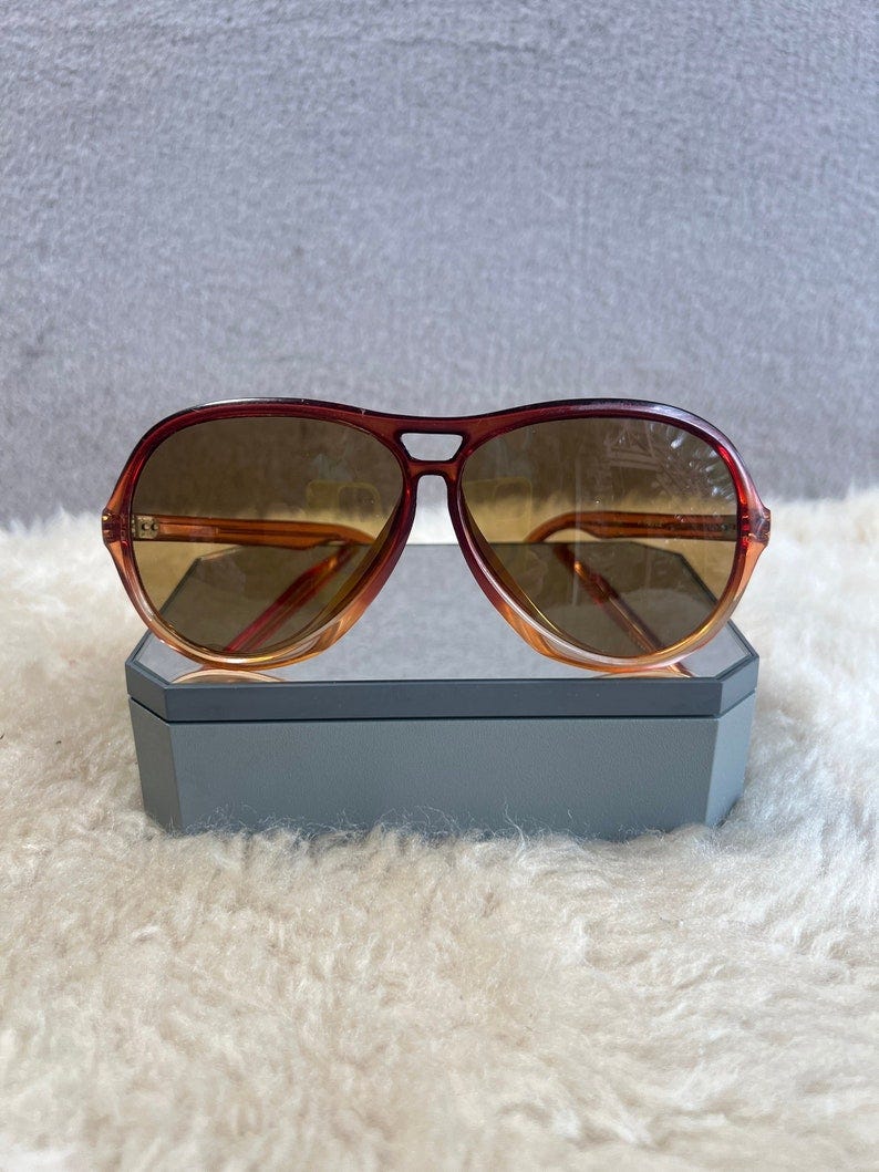 May include: A pair of brown aviator sunglasses with a tortoise shell frame. The sunglasses are sitting on a gray box.