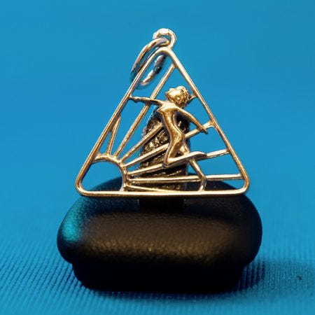 A trio of images showing naturist symbols. The first is a black-and-white line design created in 1973 by Dutch jeweler Cor Uytenhaak, depicting a nude figure within a triangular frame and rising sun. The second is a pendant version of the same symbol photographed against a blue background. The third is a yellow and blue diagonally divided flag, known as the Skinny Dipper Ensign, introduced in Alaska in 2018.