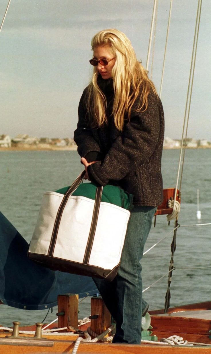 This may contain: a woman standing on the deck of a sailboat holding a large white tote bag