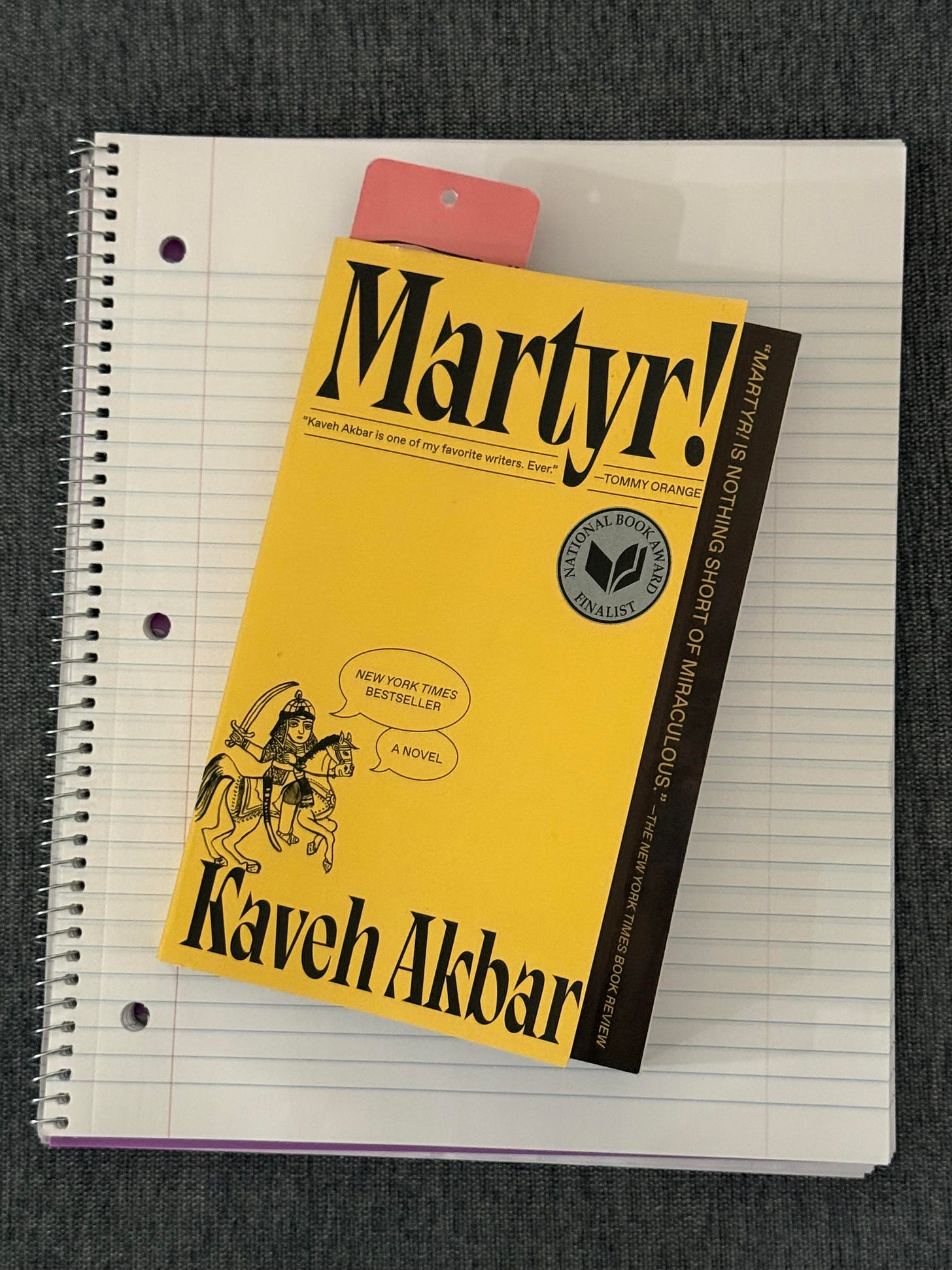 Paperback book sitting atop a lined spiral notebook, blank. 
