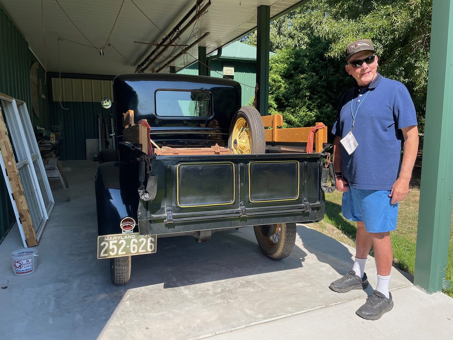 A man standing beside a black vintage truck parked in an open garage, with a Maryland license plate visible.