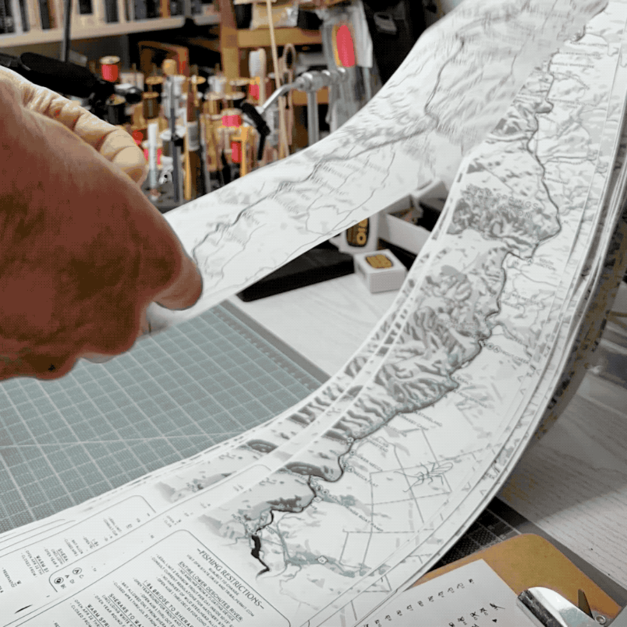 An animated timelapse image of rolling up Lower Deschutes Ribbon Maps on a fly tying desk