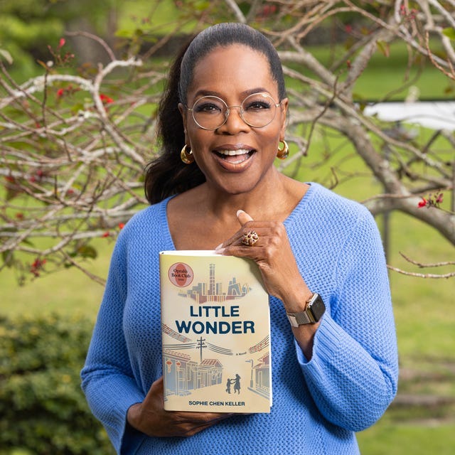 oprah winfrey in blue sweater holding the book "Little Wonder" outside.