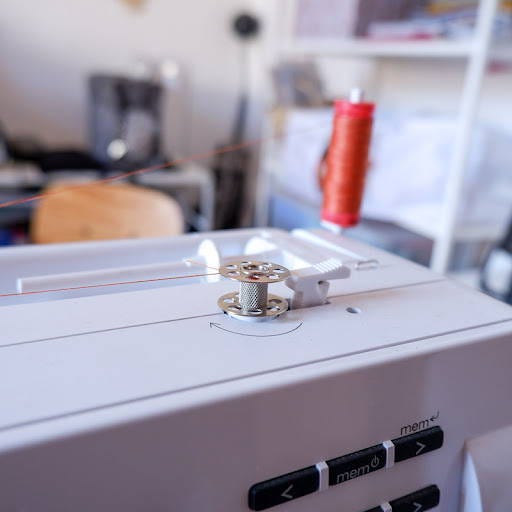 an empty bobbin on a bobbin winder pin to be threaded with orange thread