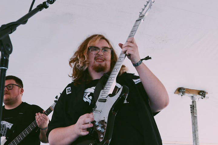 First image is a person with blonde hair surrounded by greenery and shadows. Second image is a group of four people standing together. Third image is of a person wearing glasses and playing guitar on a stage. Fourth image is of five people hugging in front of a wooded area. 