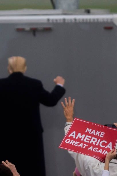 Supporter gestures with four fingers signifying another term in office as President Donald Trump acknowledges the cheers while departing after a...