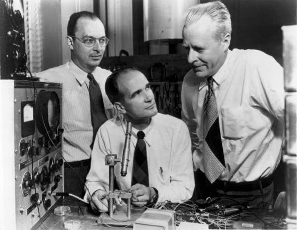 Three physicists in shirts and ties in Bell Laboratories in 1948. There's a microscope in the middle of the photo pointed at a transistor.