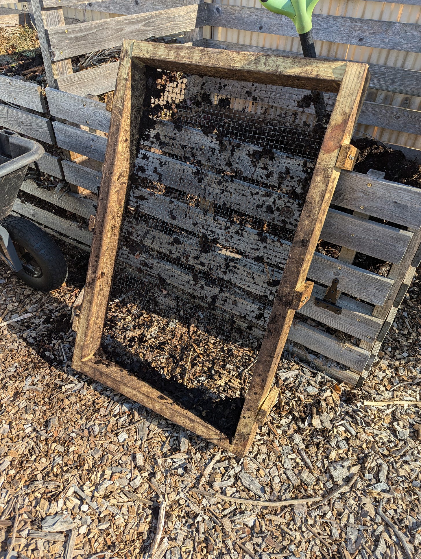 A compost sifter leans against a compost structure.  The sifter is simply a wooden frame with 1/2" mesh hardware cloth attached.  It's made to the dimension of my garden cart.