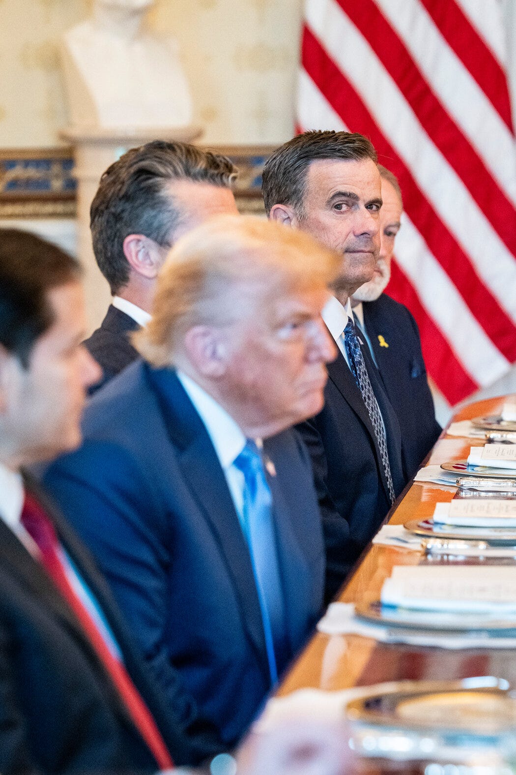 Hombres trajeados sentados en una mesa con la bandera estadounidense de fondo. Hombres trajeados sentados en una mesa con la bandera estadounidense de fondo.