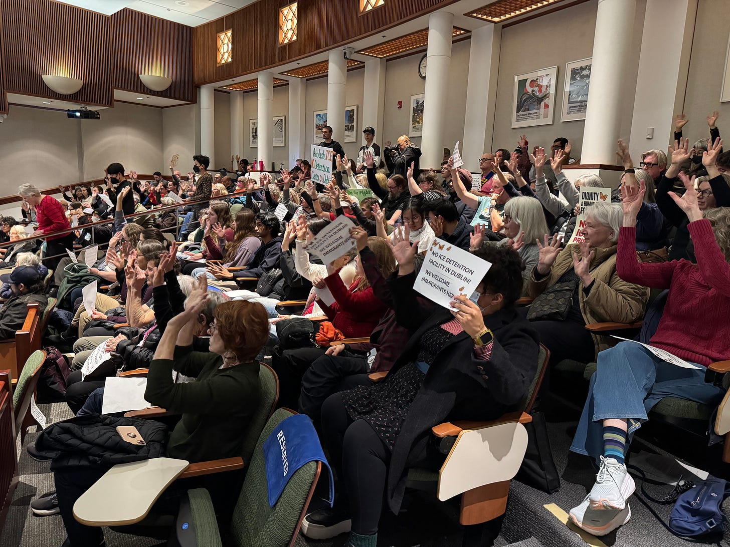 People sit in rows of desk chairs and hold signs protesting ICE People sit in rows of desk chairs and hold signs protesting ICE