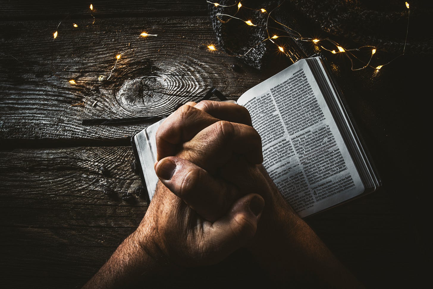 Clenched hands in prayer on a Bible resting on a piece of wood with grains showing Clenched hands in prayer on a Bible resting on a piece of wood with grains showing
