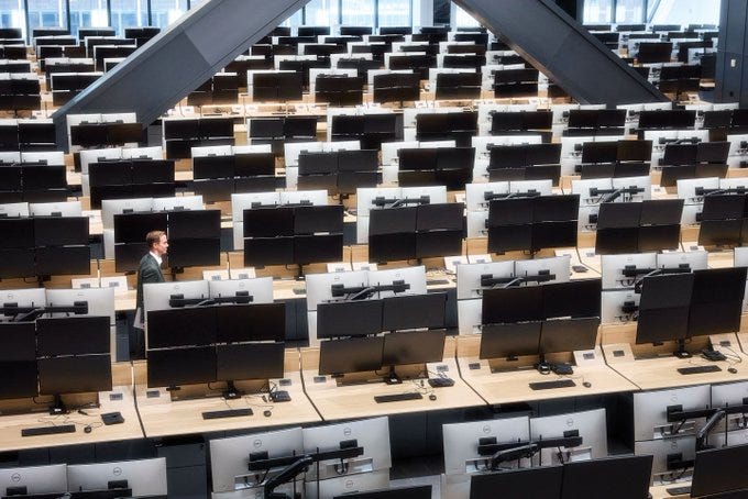 Modern office interior with rows of identical desks each equipped with multiple computer monitors and peripherals arranged in a grid pattern under a prominent triangular black structural beam spanning the ceiling large glass windows allow natural light to illuminate the space a man in a dark suit stands near one desk facing away from the camera emphasizing the expansive and organized workspace Modern office interior with rows of identical desks each equipped with multiple computer monitors and peripherals arranged in a grid pattern under a prominent triangular black structural beam spanning the ceiling large glass windows allow natural light to illuminate the space a man in a dark suit stands near one desk facing away from the camera emphasizing the expansive and organized workspace