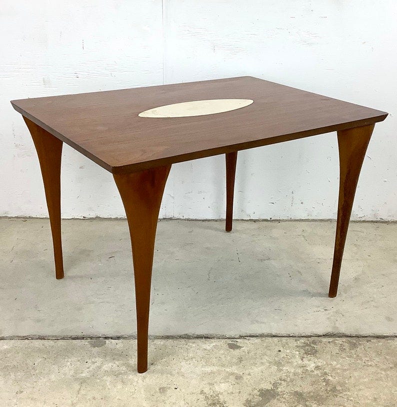 May include: A brown wooden table with a white oval inlay in the center of the tabletop. The table has four legs that are tapered and curved.
