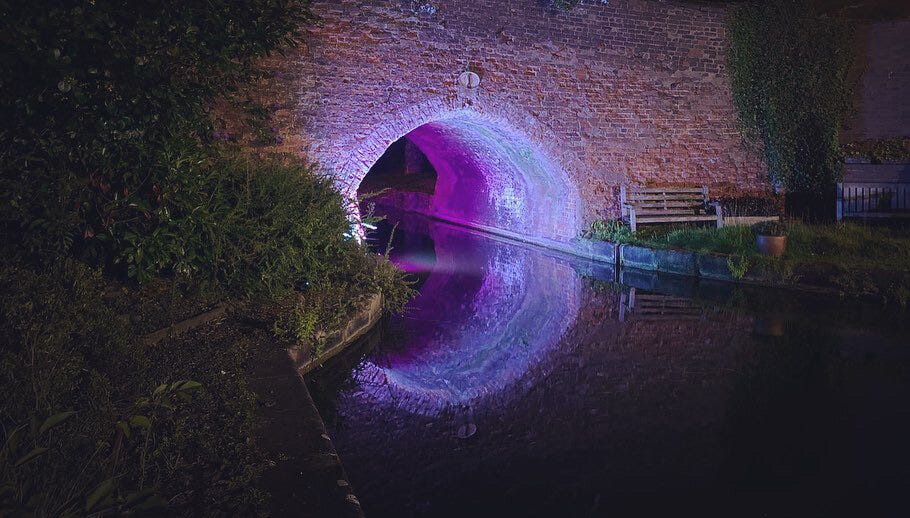 Blue and purple light reflecting off the water beneath a brick bridge to create the illusion of a circle