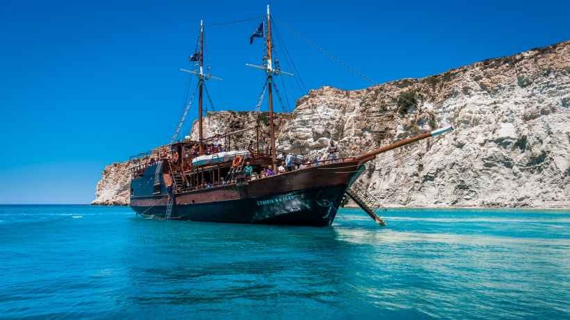 A pirate ship in front of a rocky shoreline.