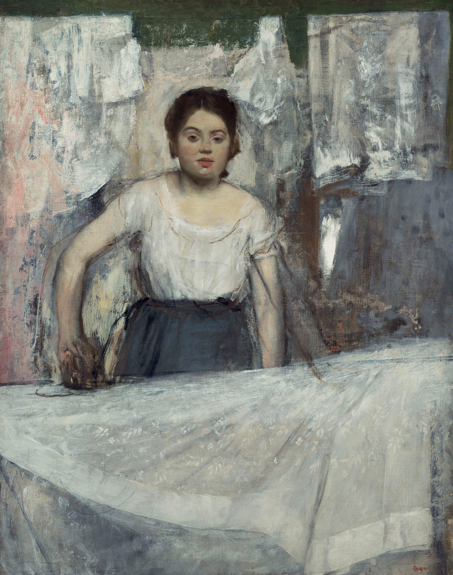 Woman with iron standing in ront of dress; other clothes hanging behind her. She is young, sleeveless blouse, looking out at viewer
