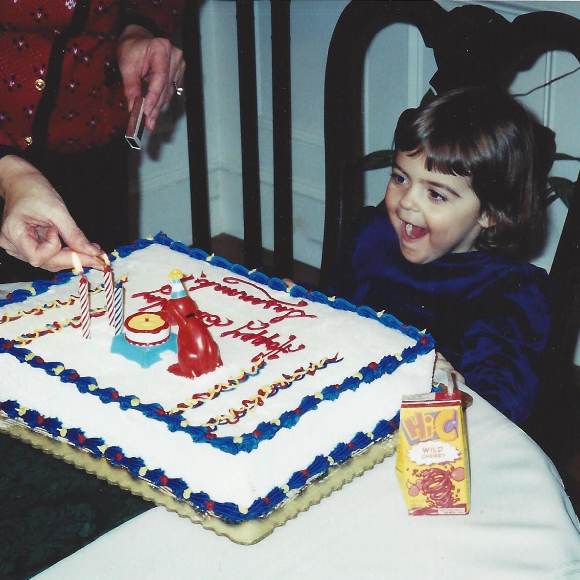 3-year-old girl smiles with anticipation as her mom lights the candles on her Clifford birthday cake 3-year-old girl smiles with anticipation as her mom lights the candles on her Clifford birthday cake