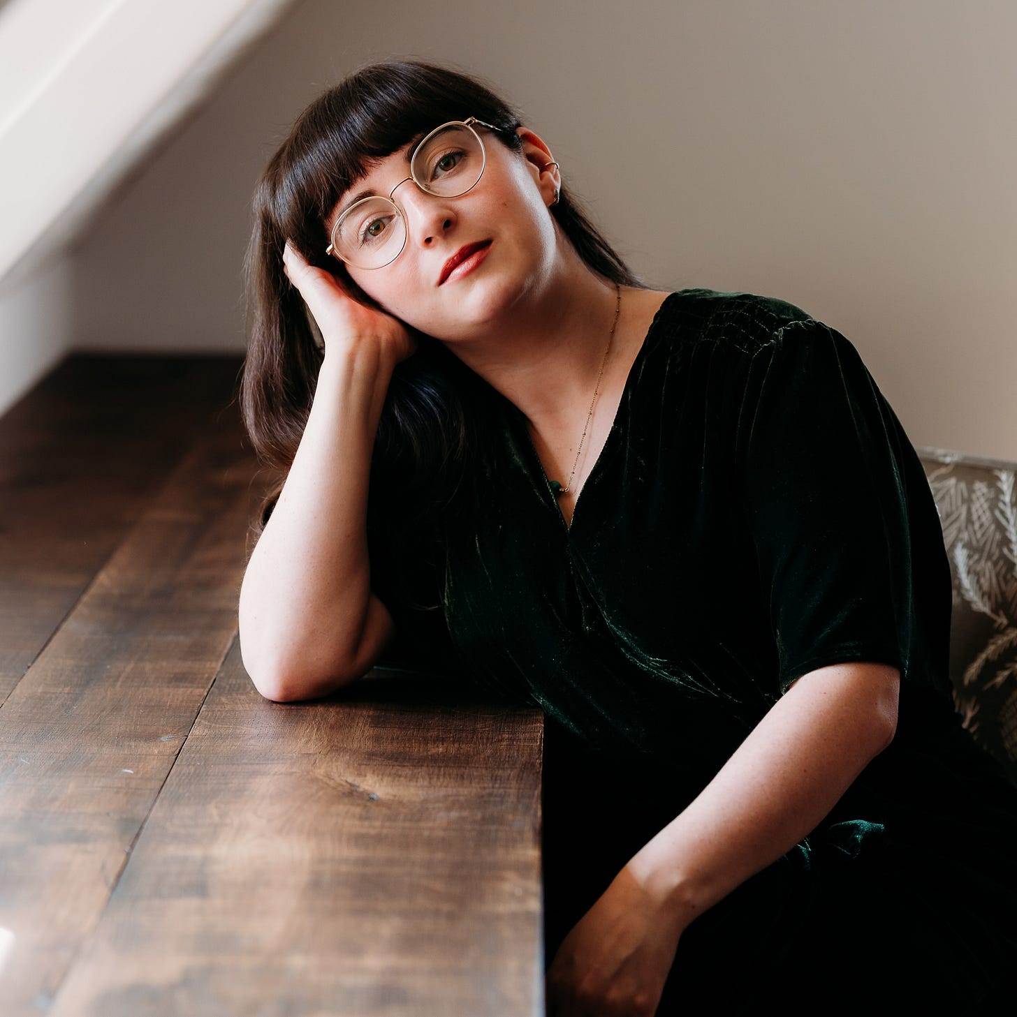 Portrait of novelist Amy Twigg seated at a wooden table, resting her head on one hand and looking toward the camera. She has dark hair, round glasses and wears a dark dress in soft natural light, photographed for a Tarot DMs interview about Spoilt Creatures, Milk, Bread, Teeth, tarot, writing and creative process. Portrait of novelist Amy Twigg seated at a wooden table, resting her head on one hand and looking toward the camera. She has dark hair, round glasses and wears a dark dress in soft natural light, photographed for a Tarot DMs interview about Spoilt Creatures, Milk, Bread, Teeth, tarot, writing and creative process.